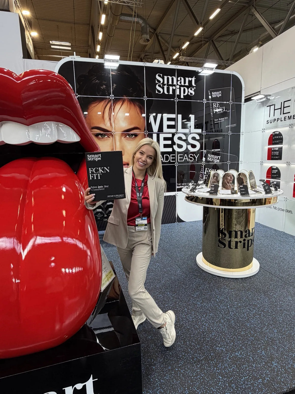 Щандът на Smart Strips на FIBO 2026 в Кьолн с огромната скулптура на червени устни и стената Wellness Made Easy