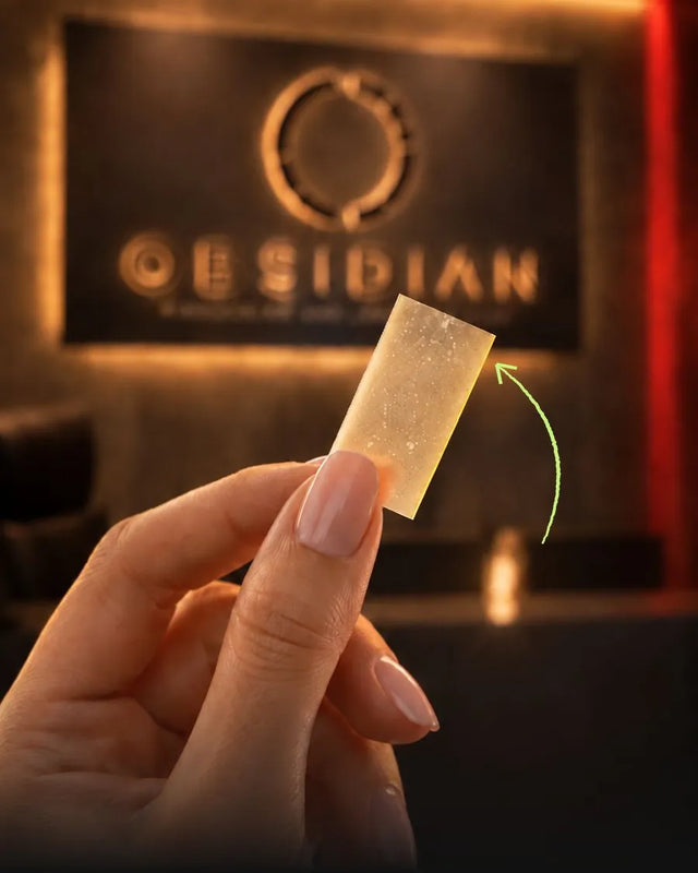 Hand holding a thin Smart Strips oral dissolvable strip in front of the Obsidian logo